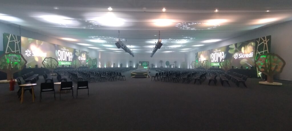 Plenária da Convenção Sicredi Aliança PR/SP 2024 com cenografia BIOMA: painéis de LED, árvores cenográficas e palco central, projeto e montagem Sonora